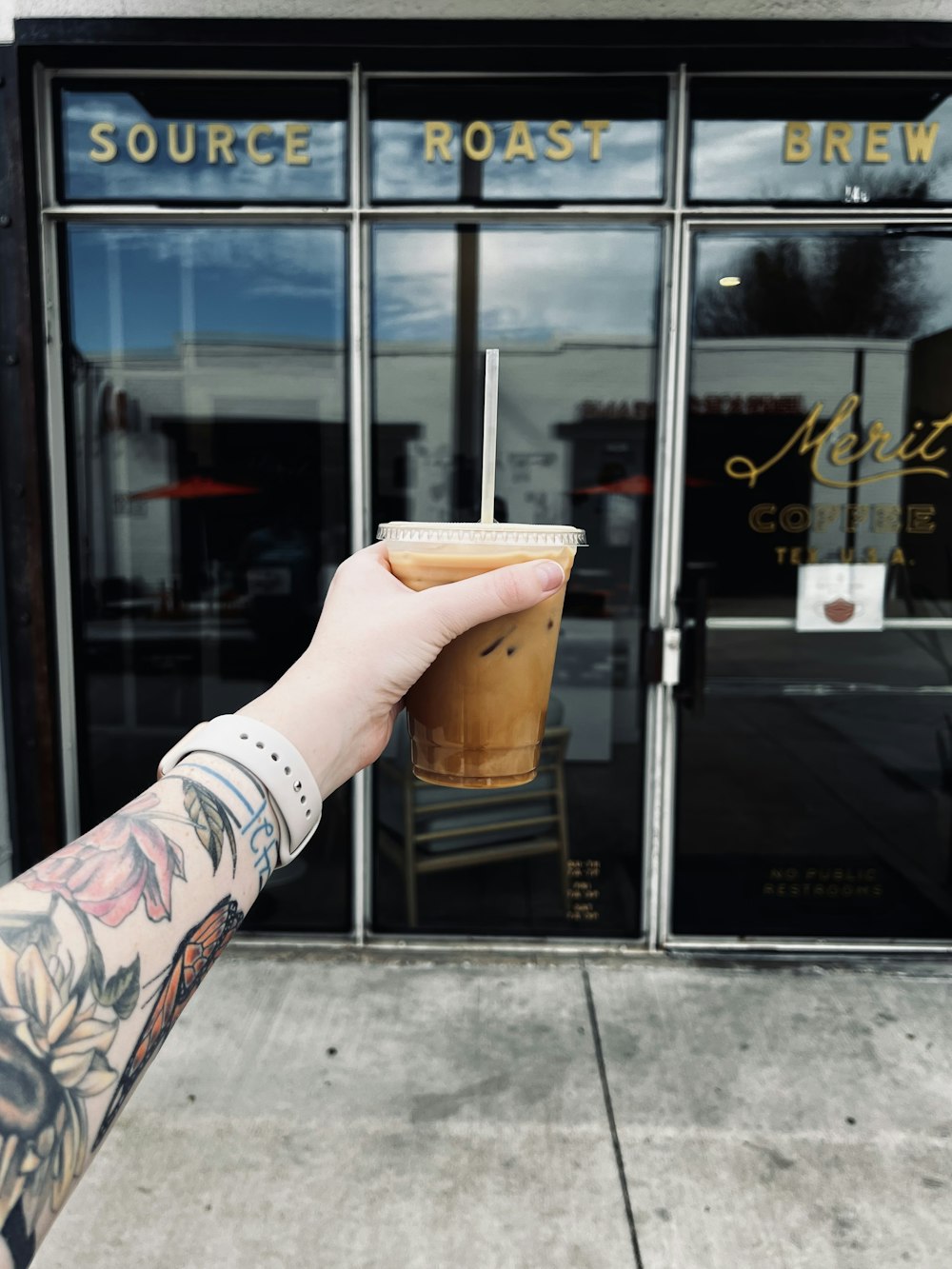 a hand holding a drink in front of a store