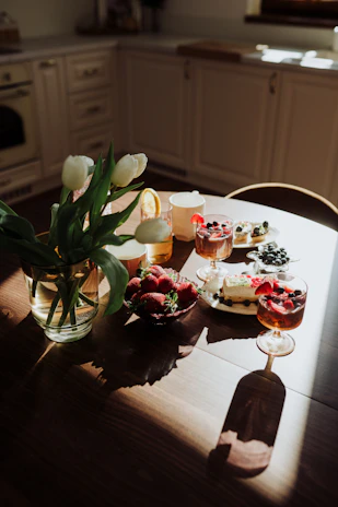 A rustic wooden table scattered with colorful cake pops and muffins, bathed in natural light.