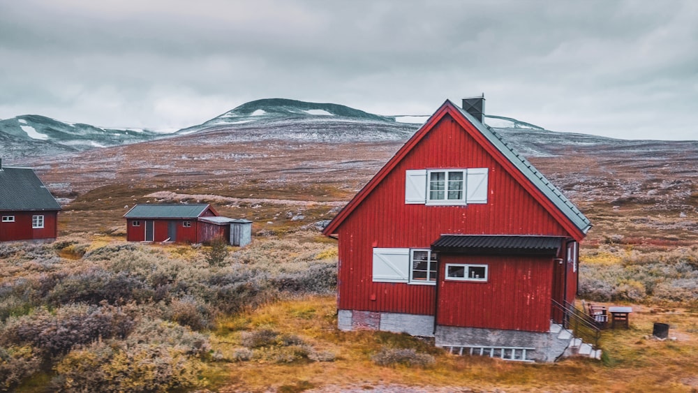 une maison rouge dans un champ avec des montagnes en arrière-plan