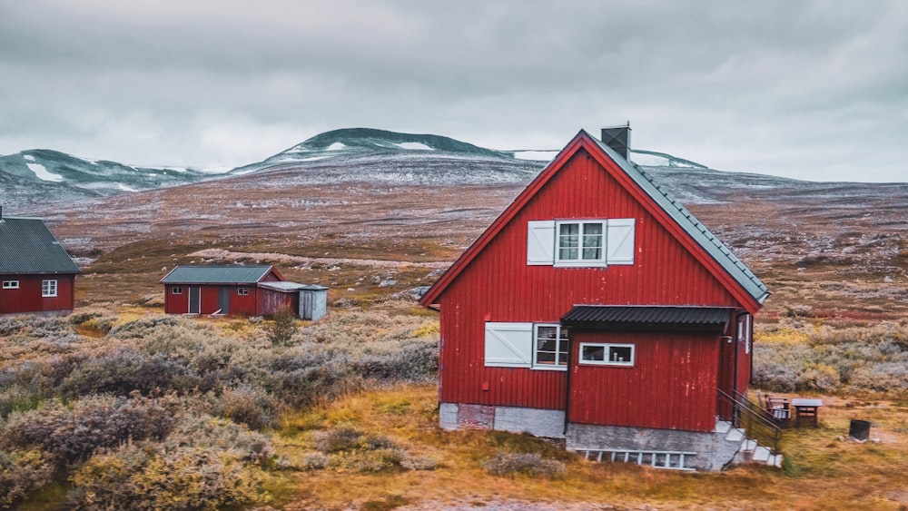 a red house in a field with mountains in the background