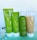 Four beauty product containers are displayed against a plain background. The containers are green and white, labeled 'JAFRA Royal Olive,' with illustrations of olives on them. There are flowers placed beside the containers for decoration.
