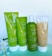 Four beauty product containers are displayed against a plain background. The containers are green and white, labeled 'JAFRA Royal Olive,' with illustrations of olives on them. There are flowers placed beside the containers for decoration.