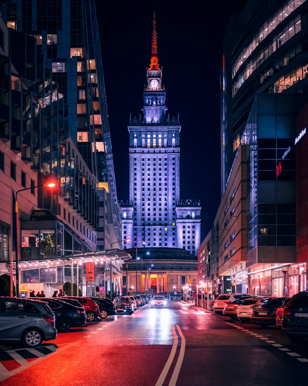 uma rua da cidade à noite com um edifício alto ao fundo