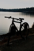 Radit's bicycle parked beside a quiet lakeside at dawn, mist rising off the water.