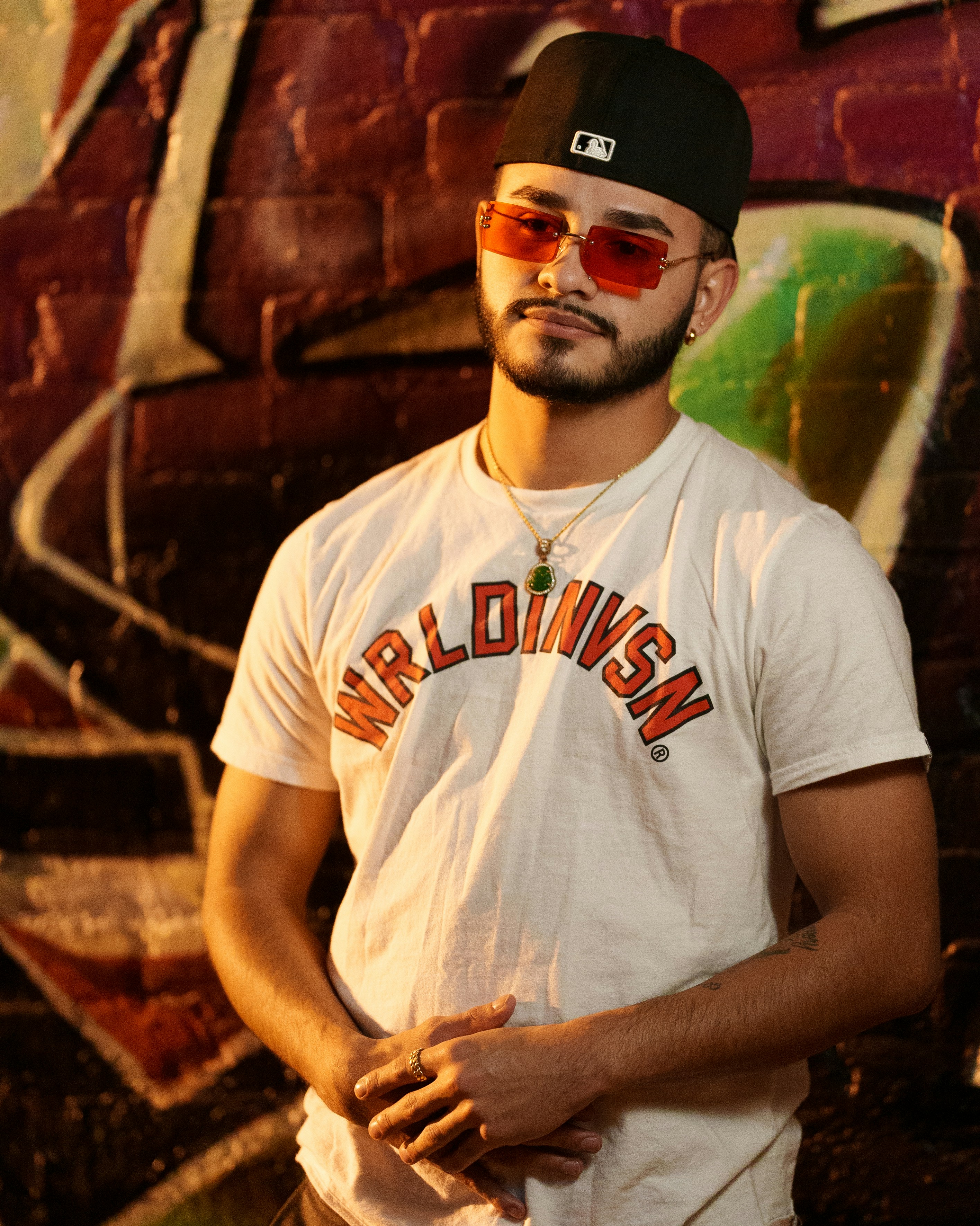 Un hombre con sombrero y gafas de sol parado frente a una pared de graffiti