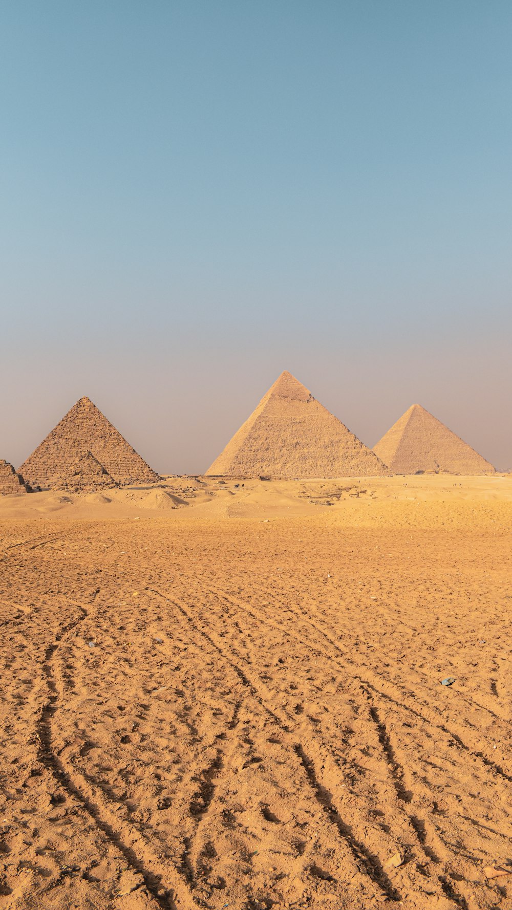 three pyramids in the desert with tracks in the sand