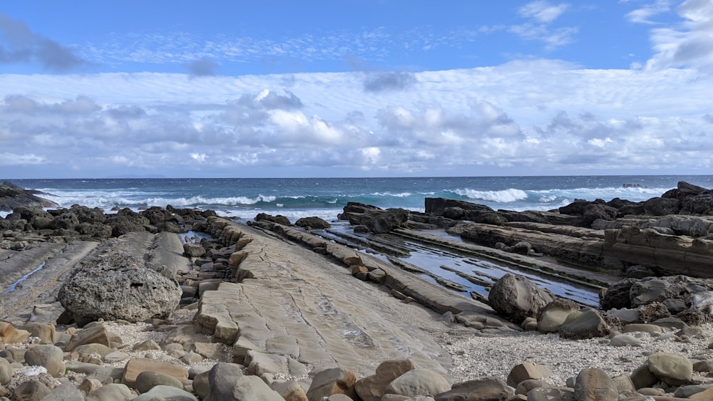 a sandy beach with rocks and water in the background