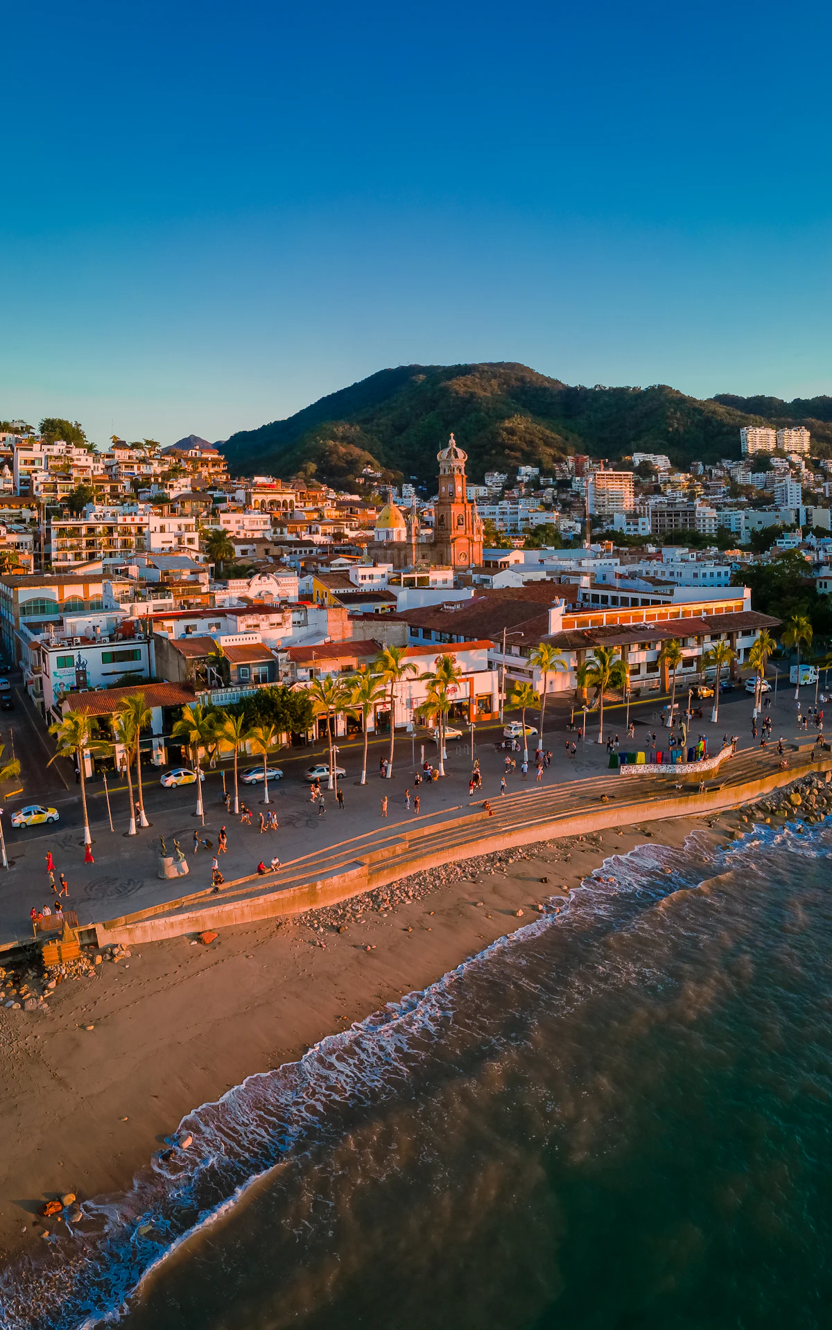 Aerial view of the Puerto Vallarta waterfront at sunset, with the beach, pier and the Church of Our Lady of Guadalupe in the town behind