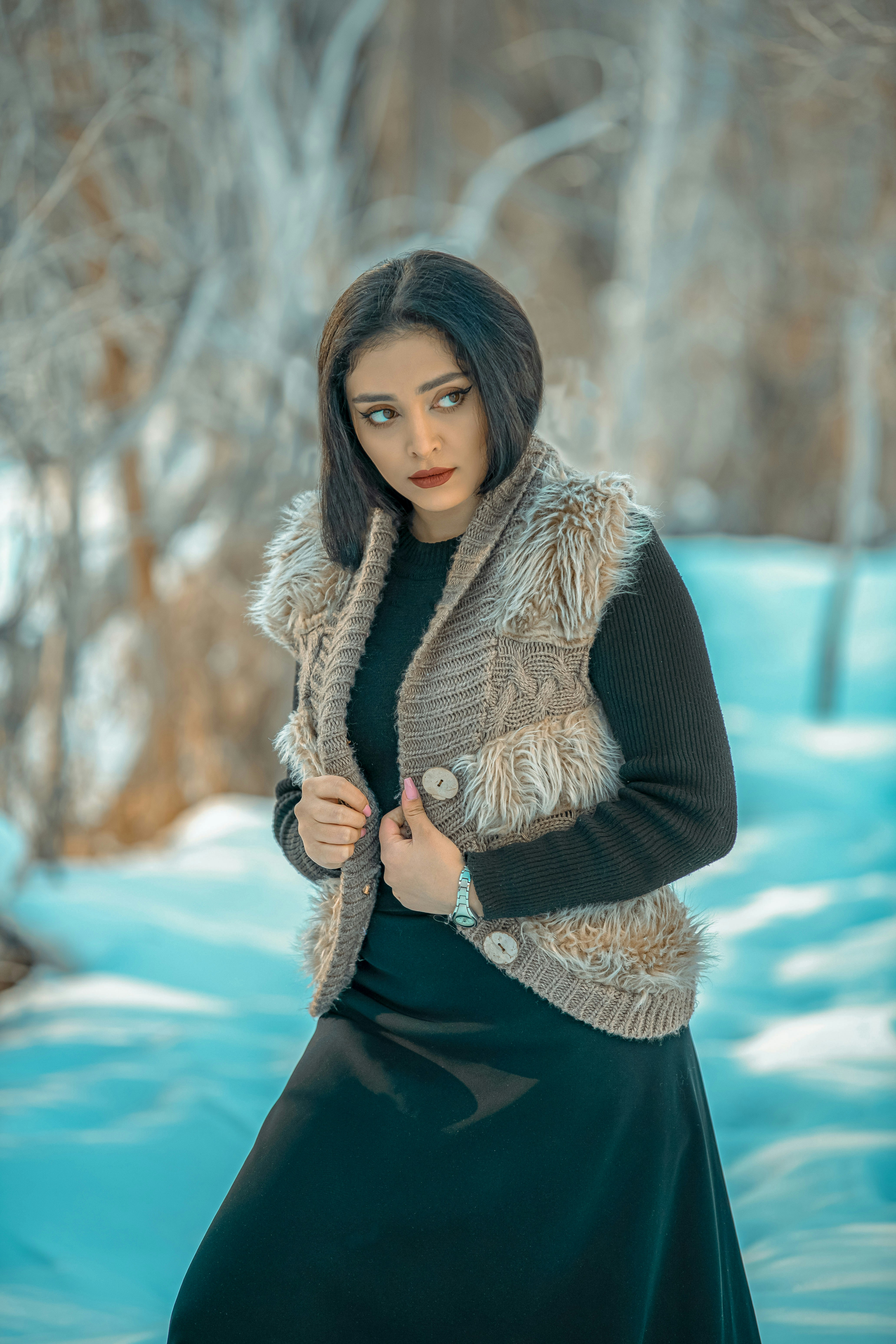 a woman standing in the snow wearing a fur vest
