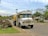 A delivery truck parked in front of a rural home with a propane tank in the yard.