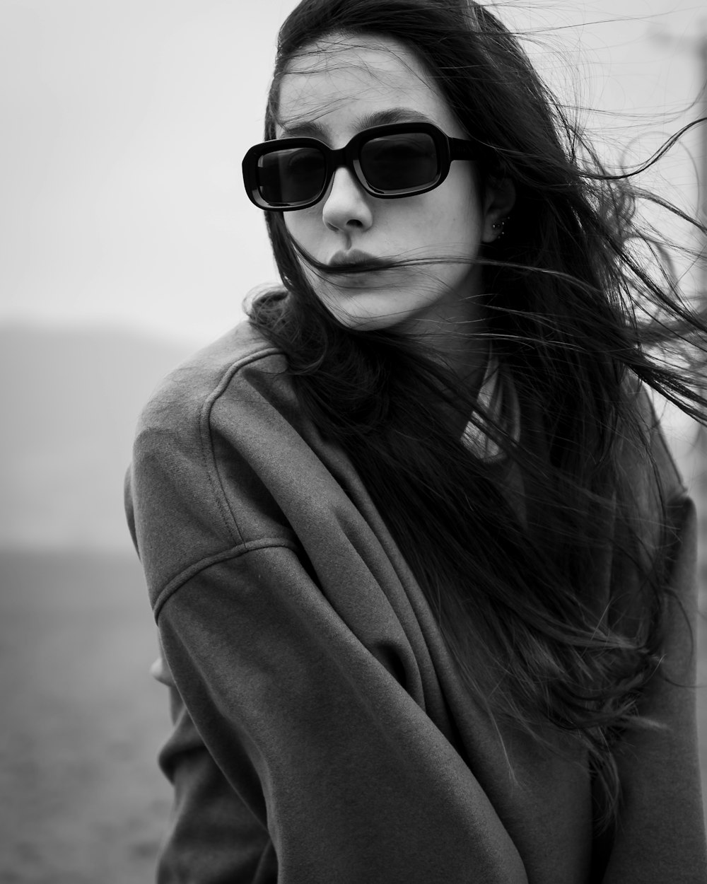 a woman with long hair wearing sunglasses and a hoodie