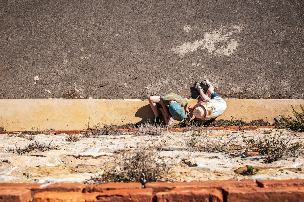a couple of people laying on top of a cement wall