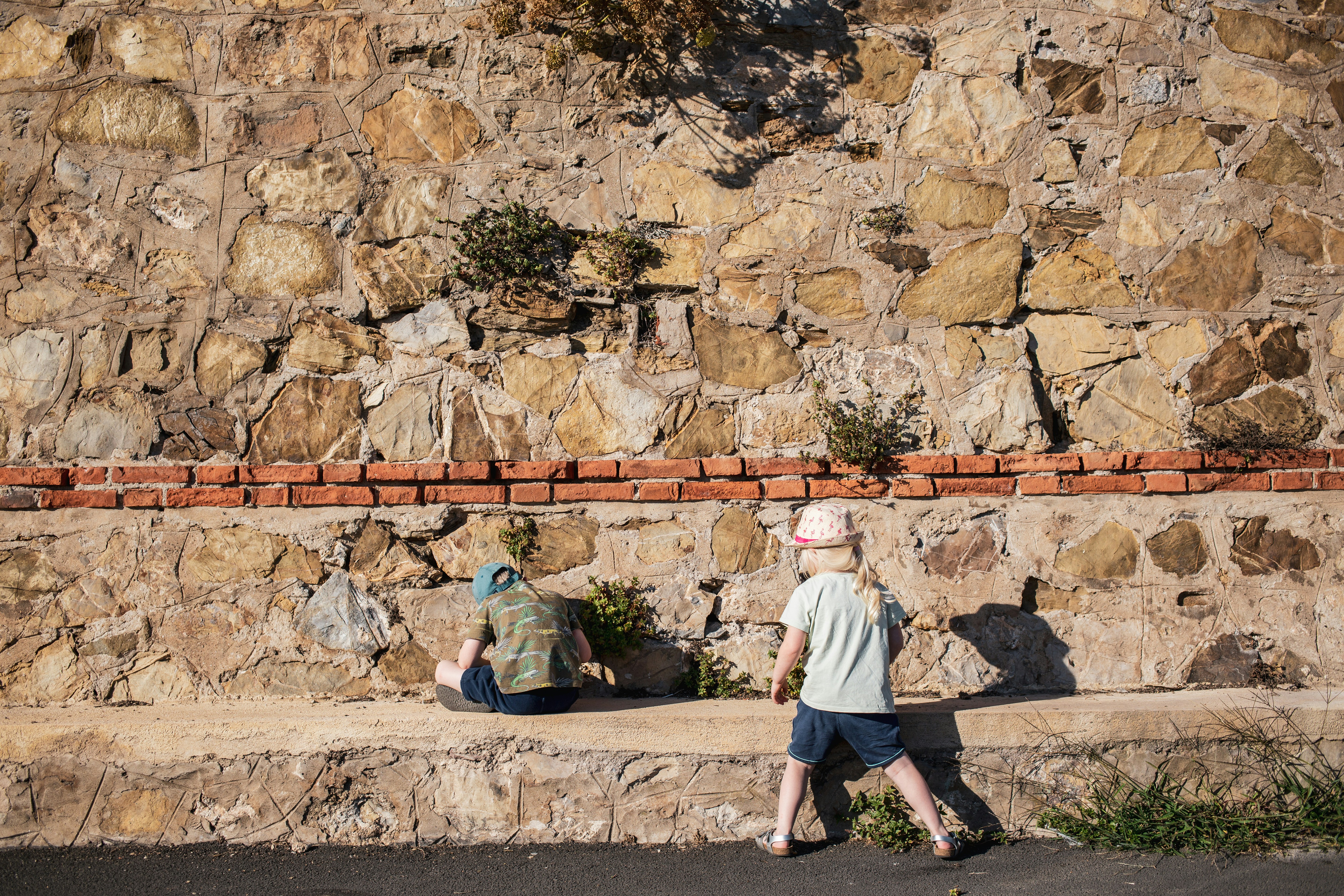 Un par de personas caminando más allá de un muro de piedra