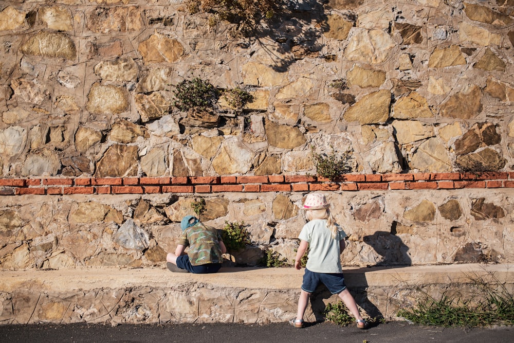 a couple of people walking past a stone wall