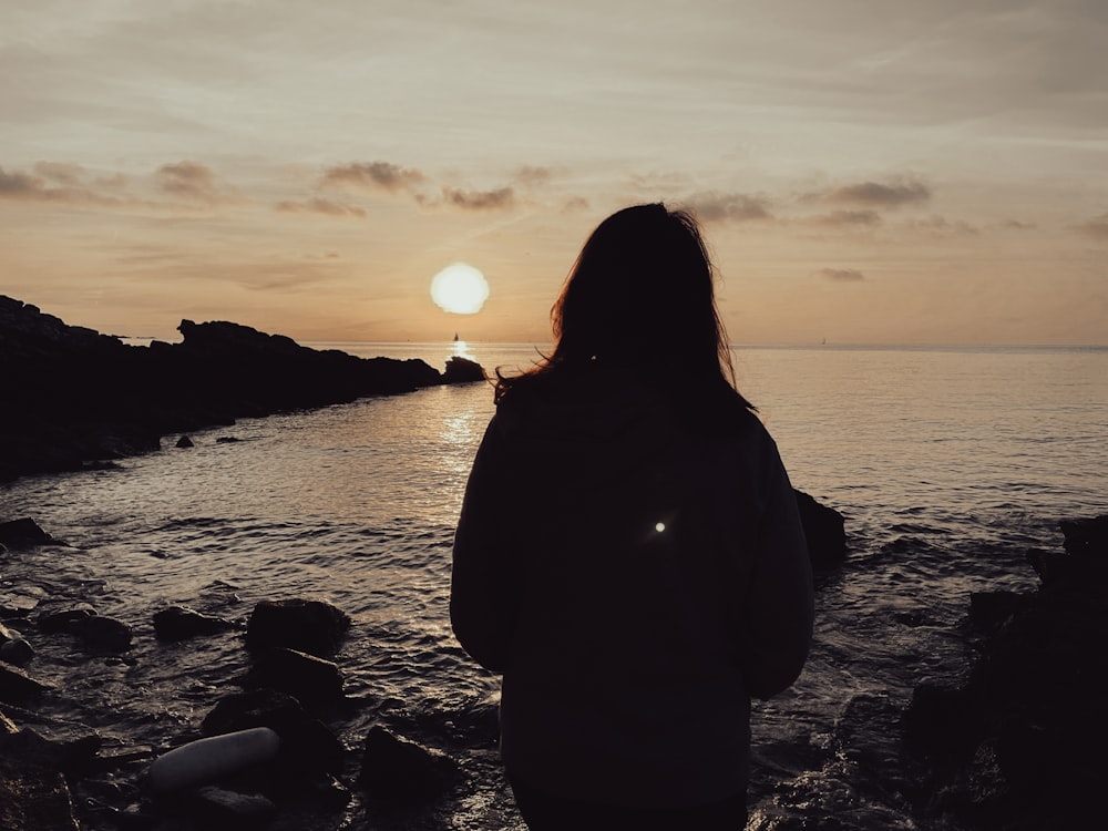 Una donna in piedi su una spiaggia rocciosa che guarda il tramonto