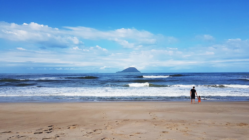 a man standing on top of a sandy beach next to the ocean