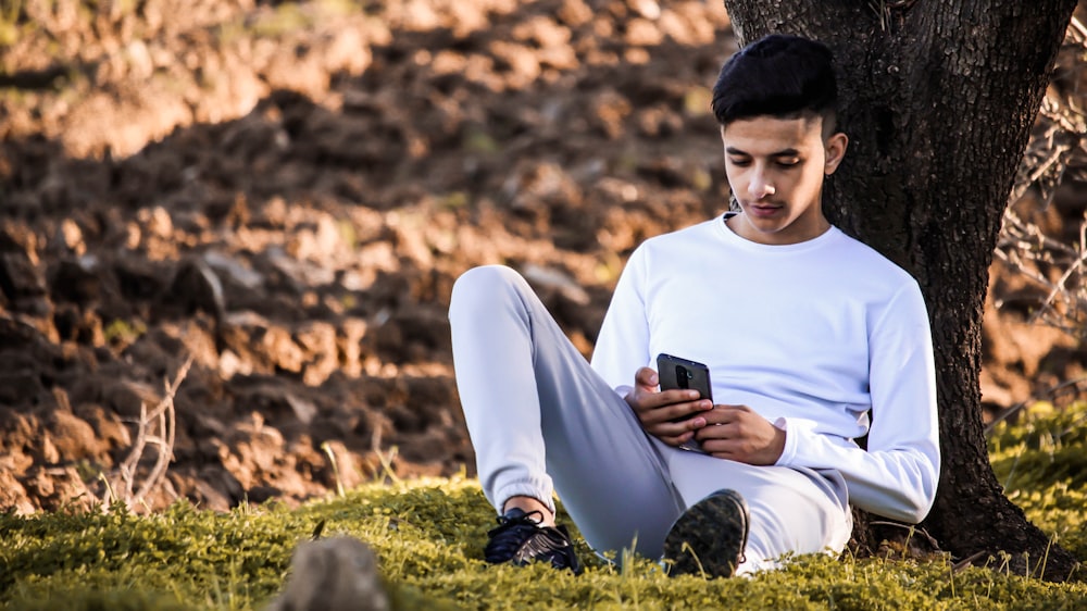 a man sitting in the grass looking at his cell phone