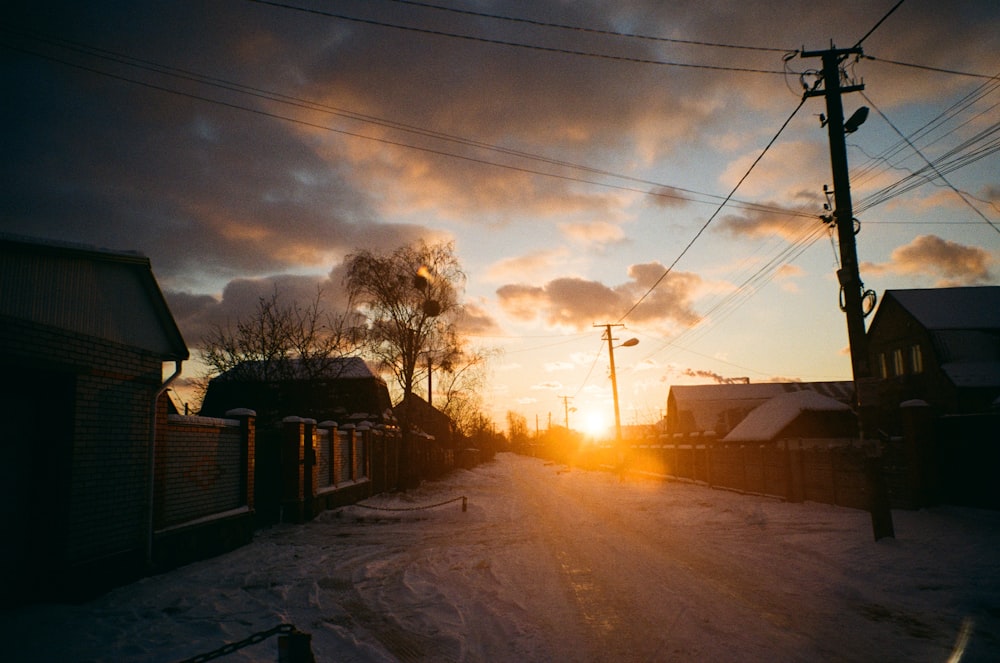 the sun is setting on a snowy street