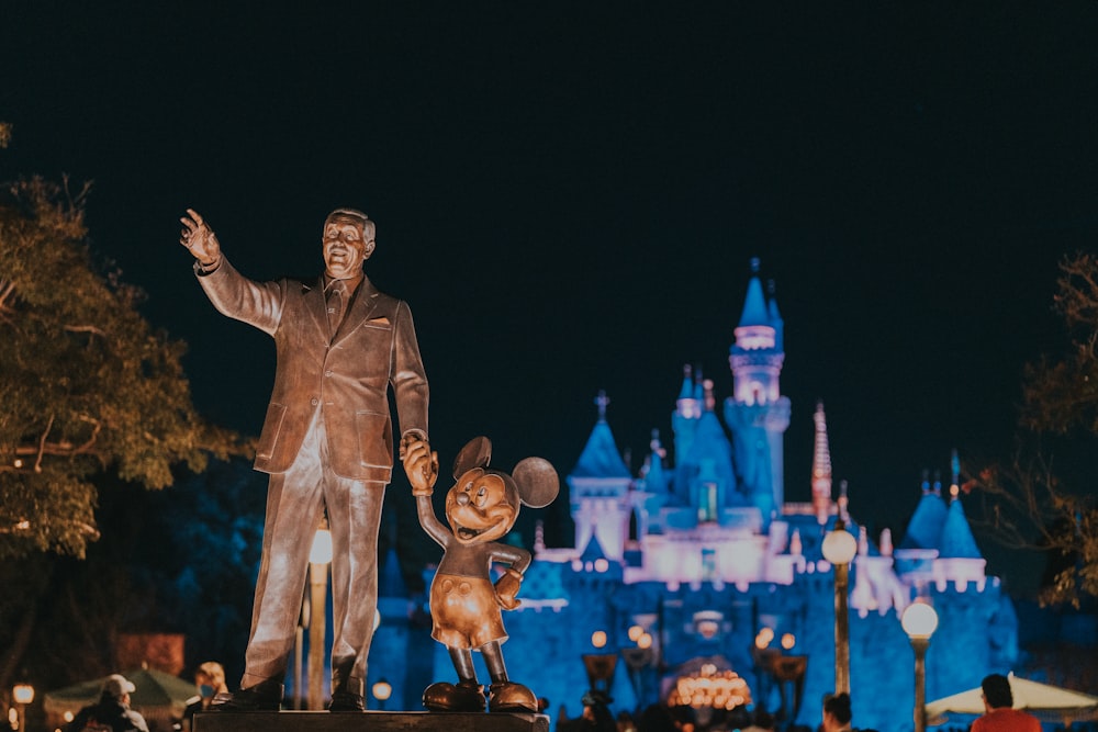 a statue of walt and mickey mouse in front of a castle