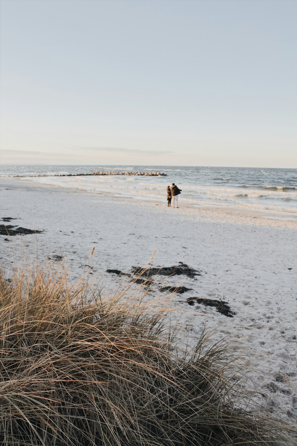 a couple of people walking on top of a sandy beach