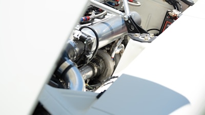 A close-up view of an engine compartment featuring polished metal components, piping, and various mechanical parts. The focus is on the metallic surfaces with bright lighting, highlighting the clean and well-maintained appearance.