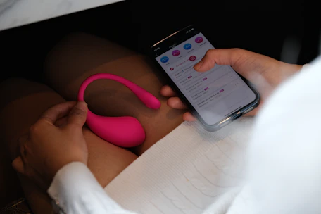 Close-up of a woman’s hand holding a smartphone showing a coaching app interface with soft pink accents.