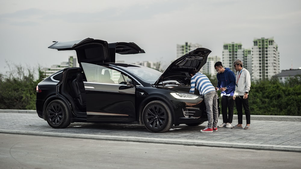 a couple of people standing next to a black car