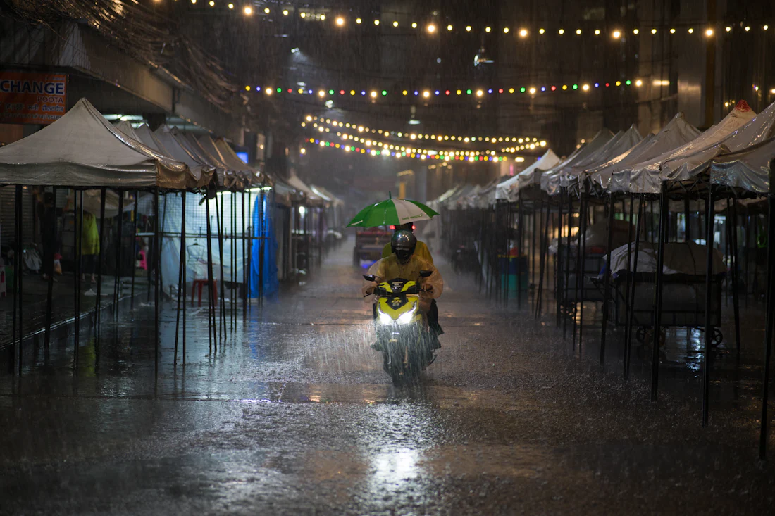 คนขี่มอเตอร์ไซค์กางร่มฝ่าฝนหนักในตลาดกลางคืนกรุงเทพฯ