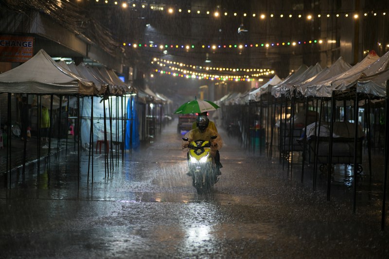Person riding motorcycle down a rain soaked street in Asia