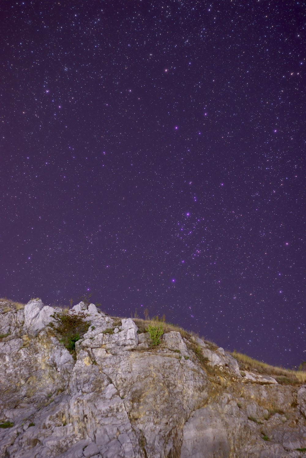 the night sky is filled with stars above a rocky hill