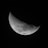A crescent moon with detailed craters and surface textures against a dark, black background. The lunar surface appears intricate and textured, highlighting the contrast between the illuminated and shadowed parts.