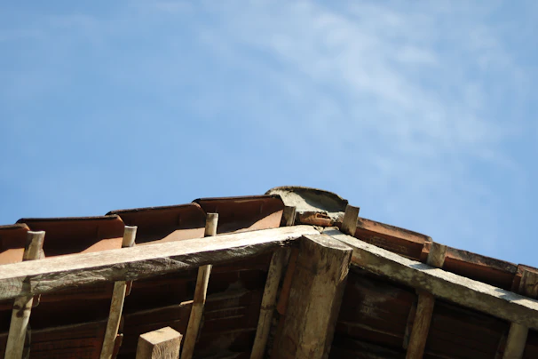 A panoramic view of a rustic house with a wooden beam roof structure partially covered with tiles.