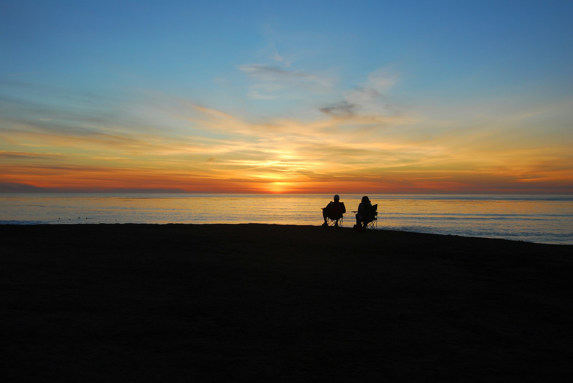 A couple sitting on benches, watching the sunset by the cliff, overlooking the ocean