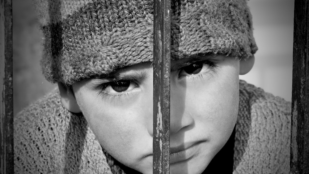 a young boy wearing a hat behind bars