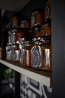 Jars of various condiments neatly displayed on a kitchen shelf with warm lighting