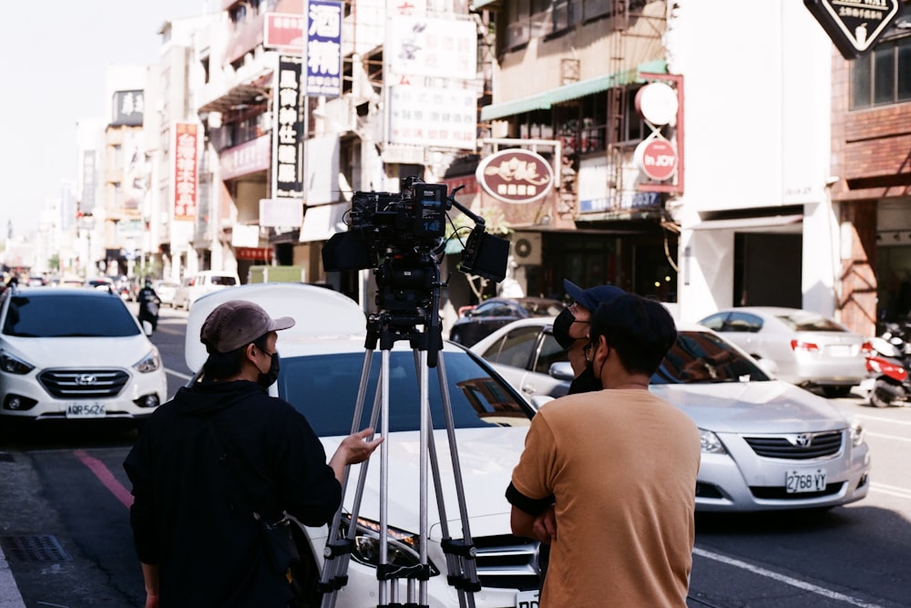 two men standing on a street with a camera on a tripod