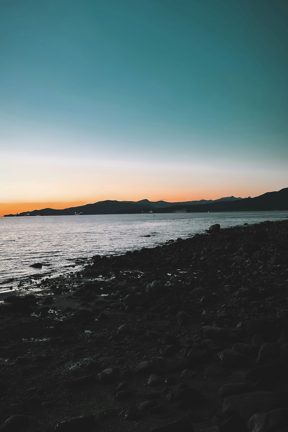 a person standing on a rocky beach at sunset