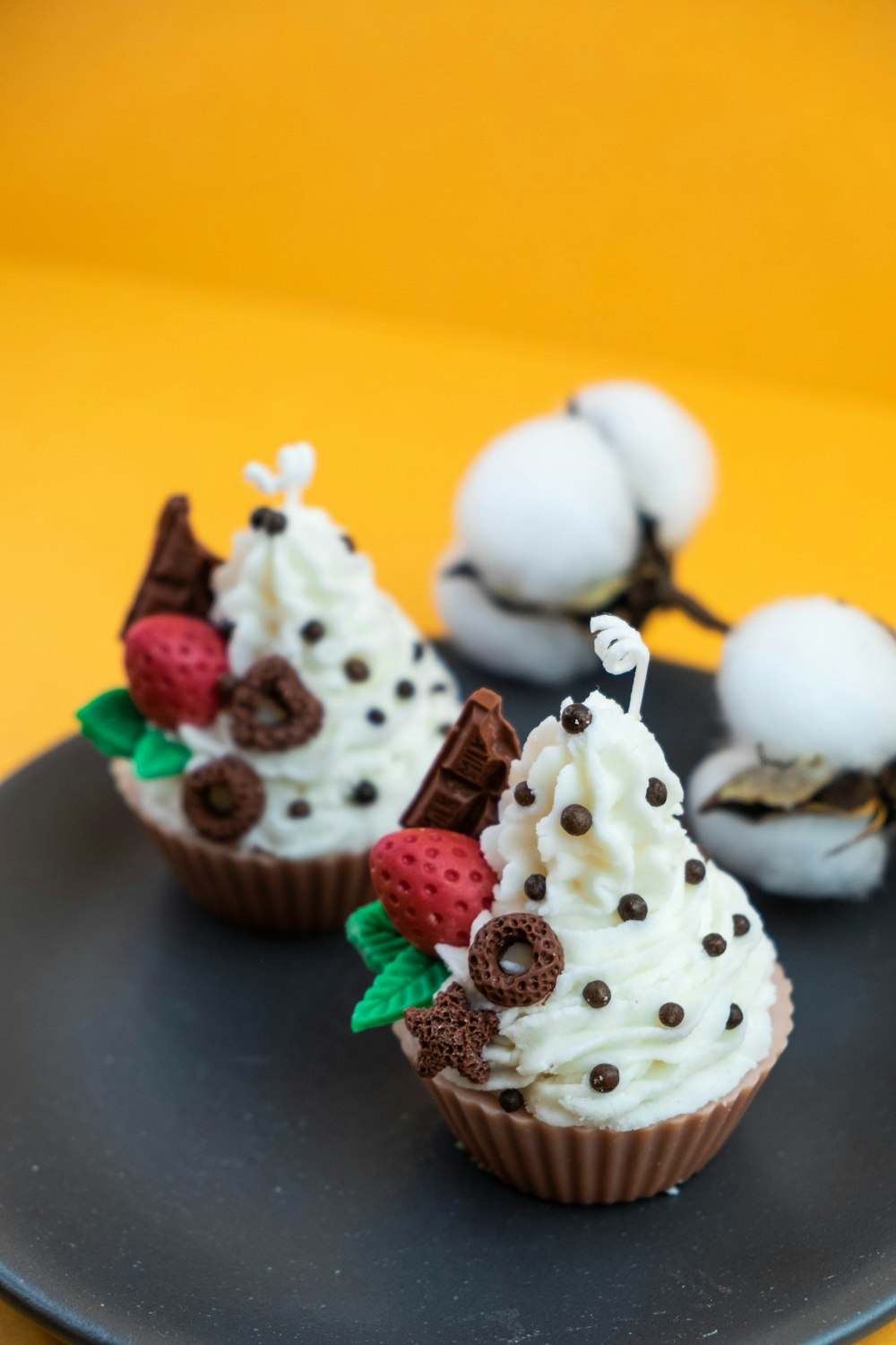 two cupcakes with white frosting and strawberries on a black plate