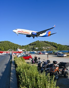 a large jetliner flying over a lush green hillside