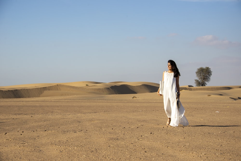 a woman in a white dress walking across a desert