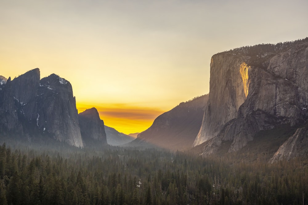 the sun is setting over the mountains and trees