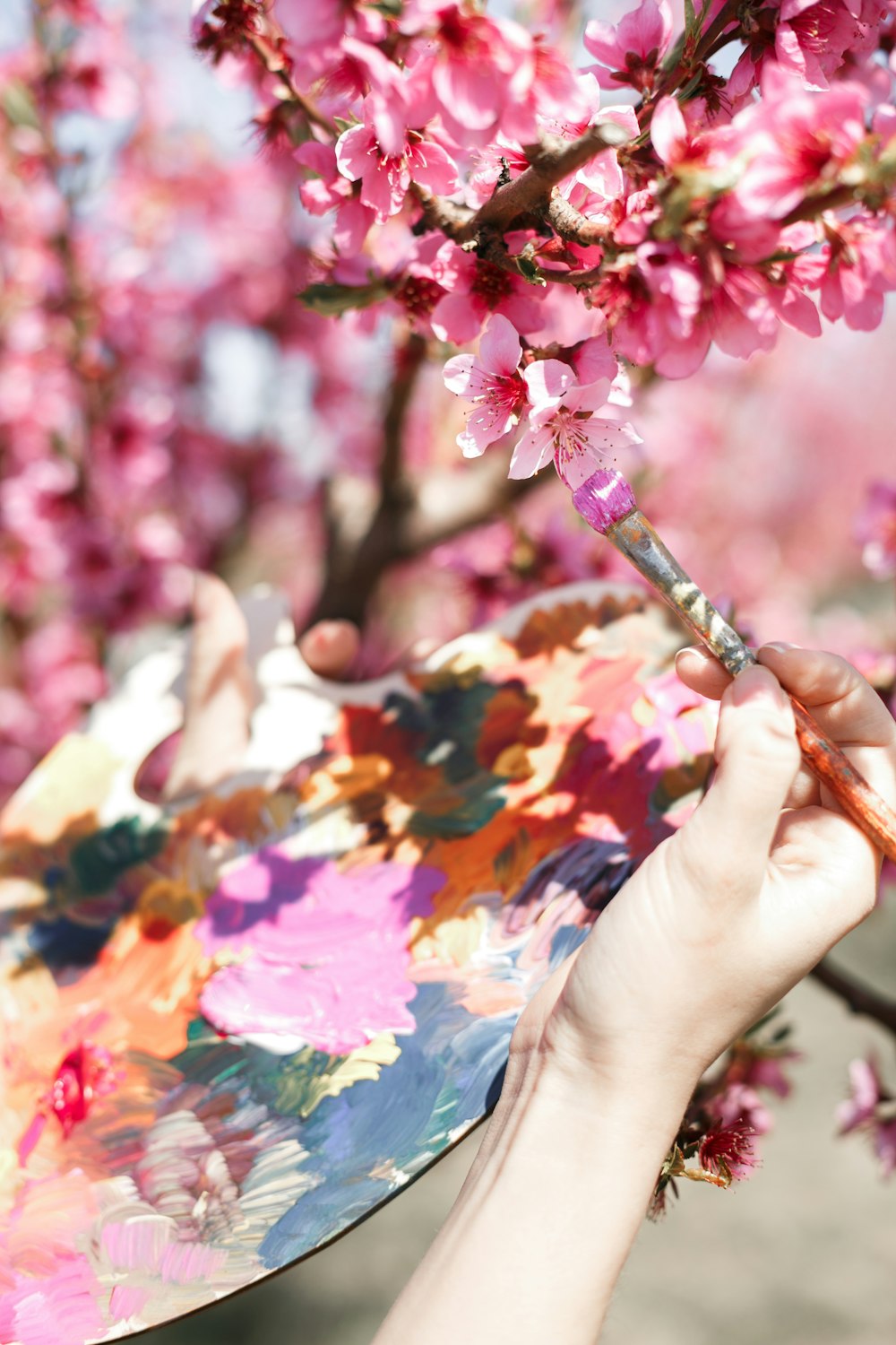 a person holding a paintbrush in front of a flowering tree