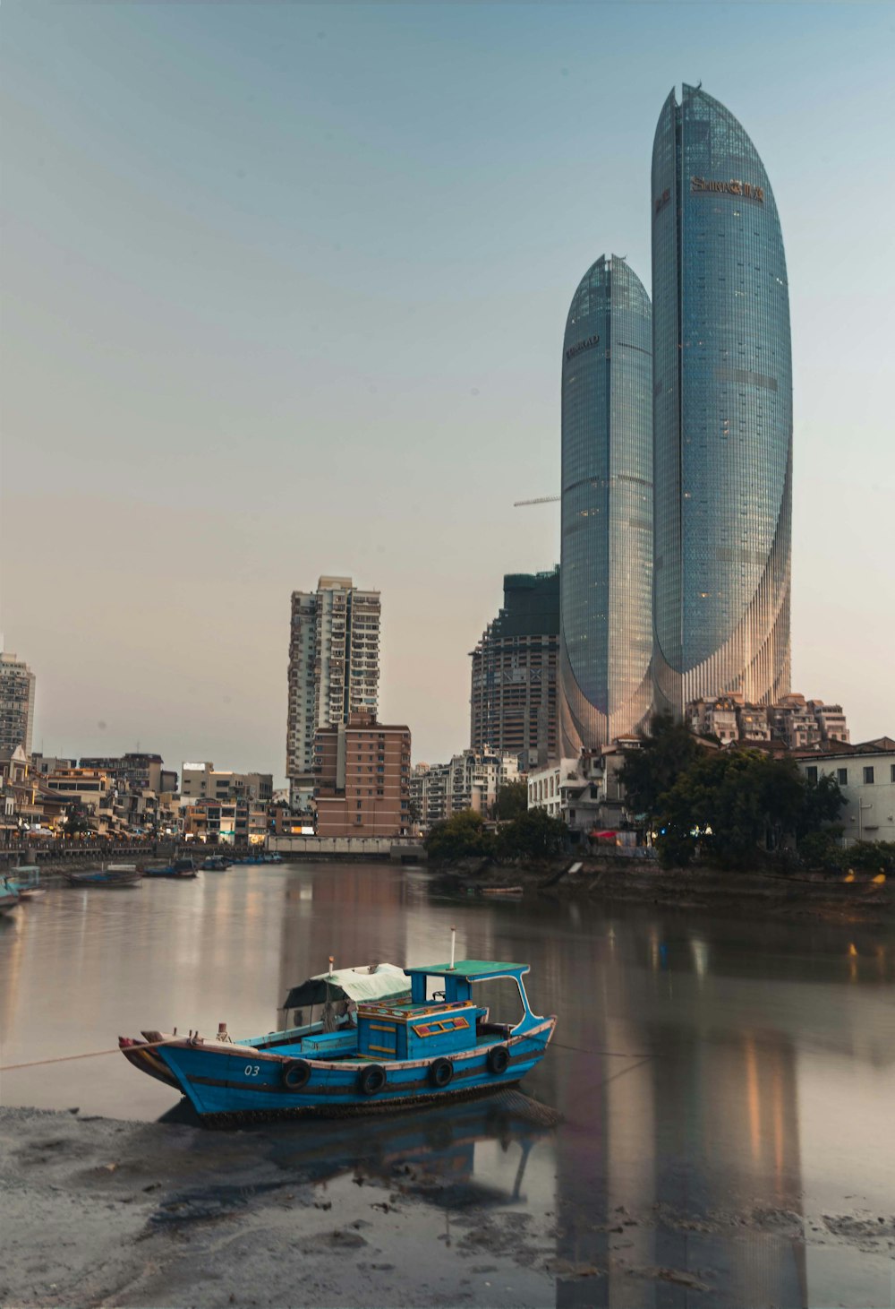 a blue boat floating on top of a river next to tall buildings