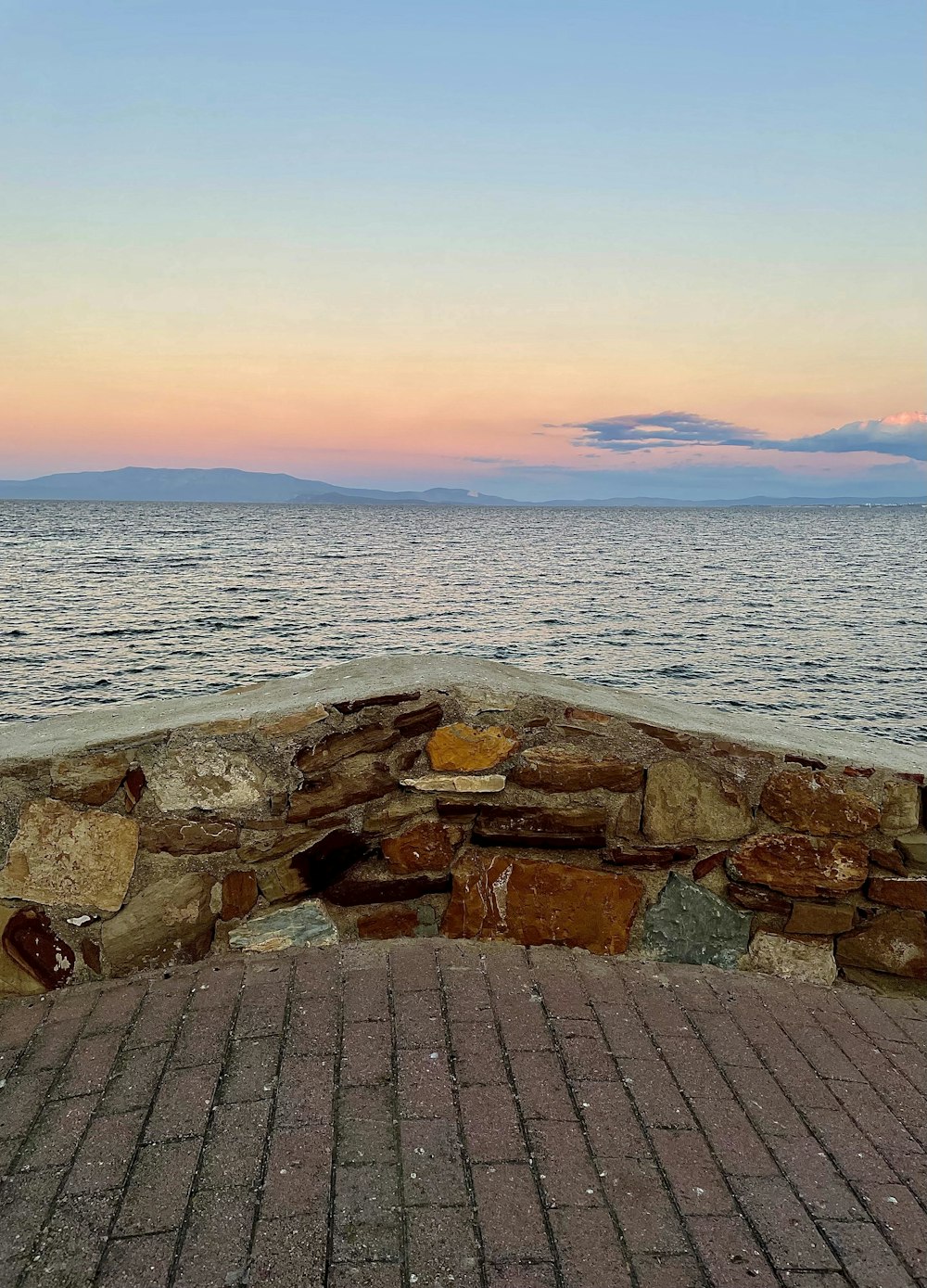 a bench sitting on top of a brick walkway near the ocean