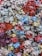 A dense cluster of fabric flowers in various colors, including blue, pink, green, lavender, and red. The flowers are layered with frayed edges, giving them a textured and somewhat rustic appearance.