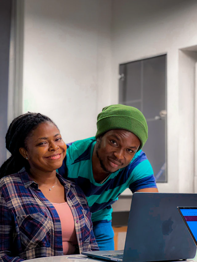 A woman and a man leaning over a laptop together and smiling.
