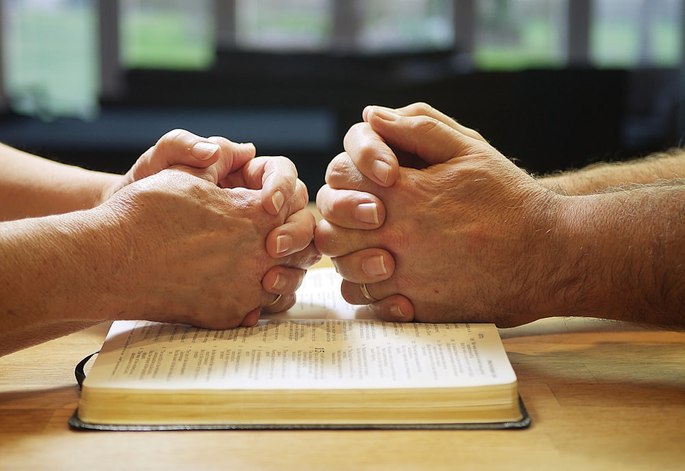 two people holding hands over a book on a table