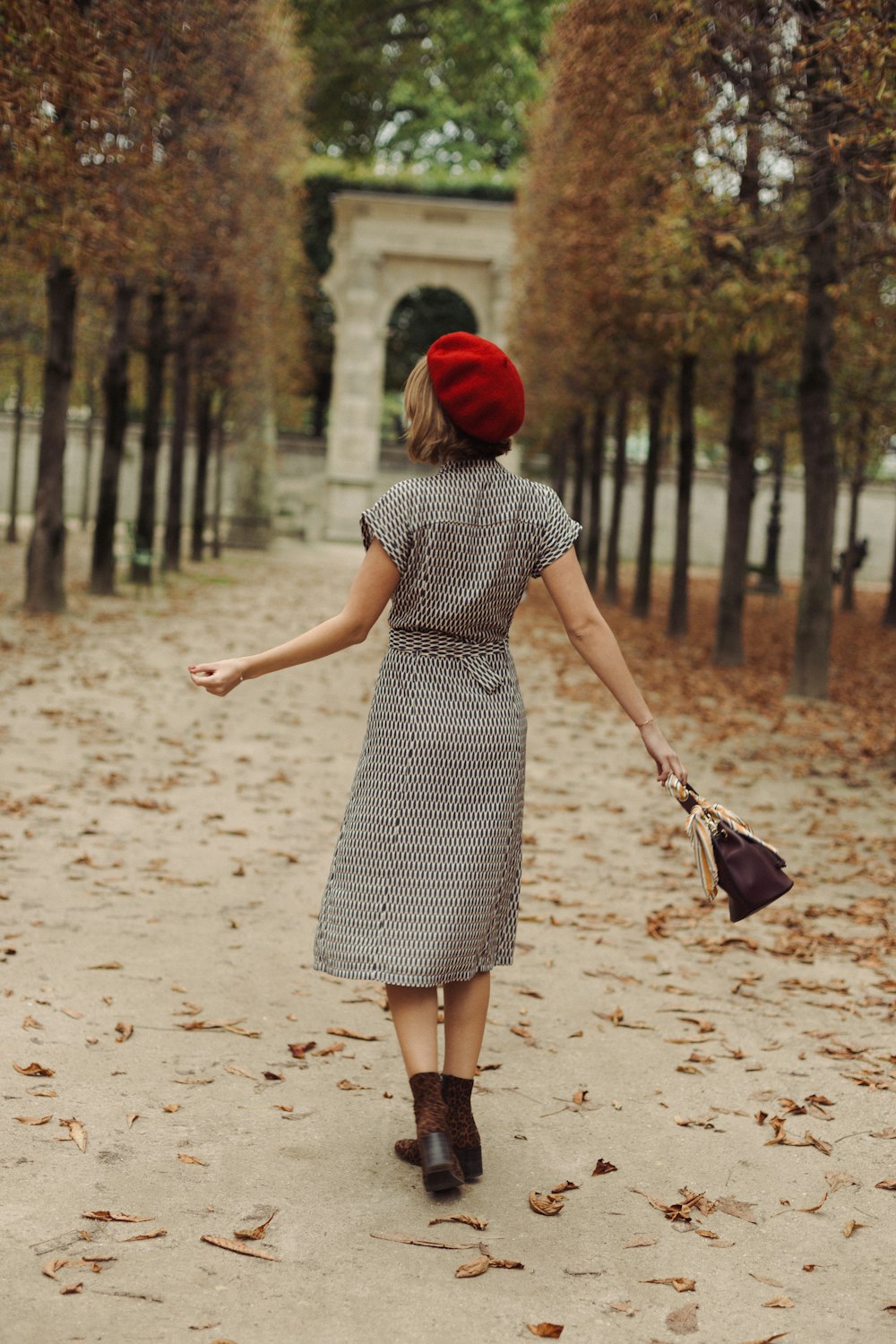 a woman in a dress and a red hat walking down a path