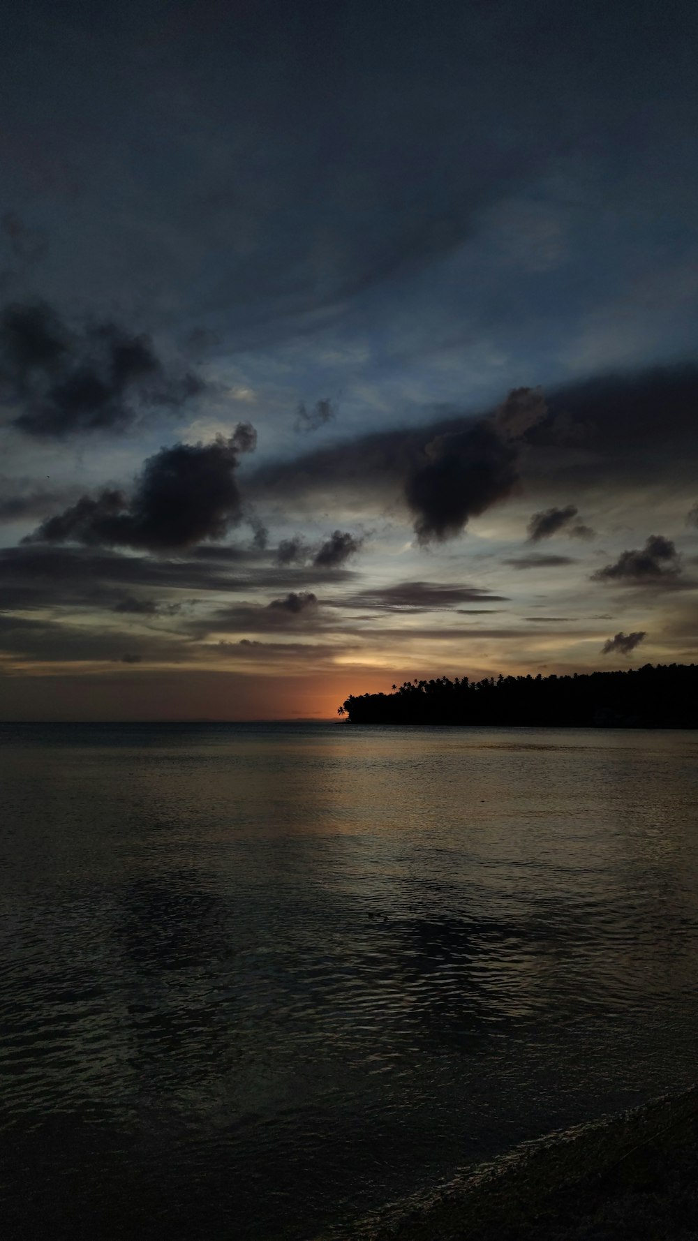 the sun is setting over the ocean with a small island in the distance