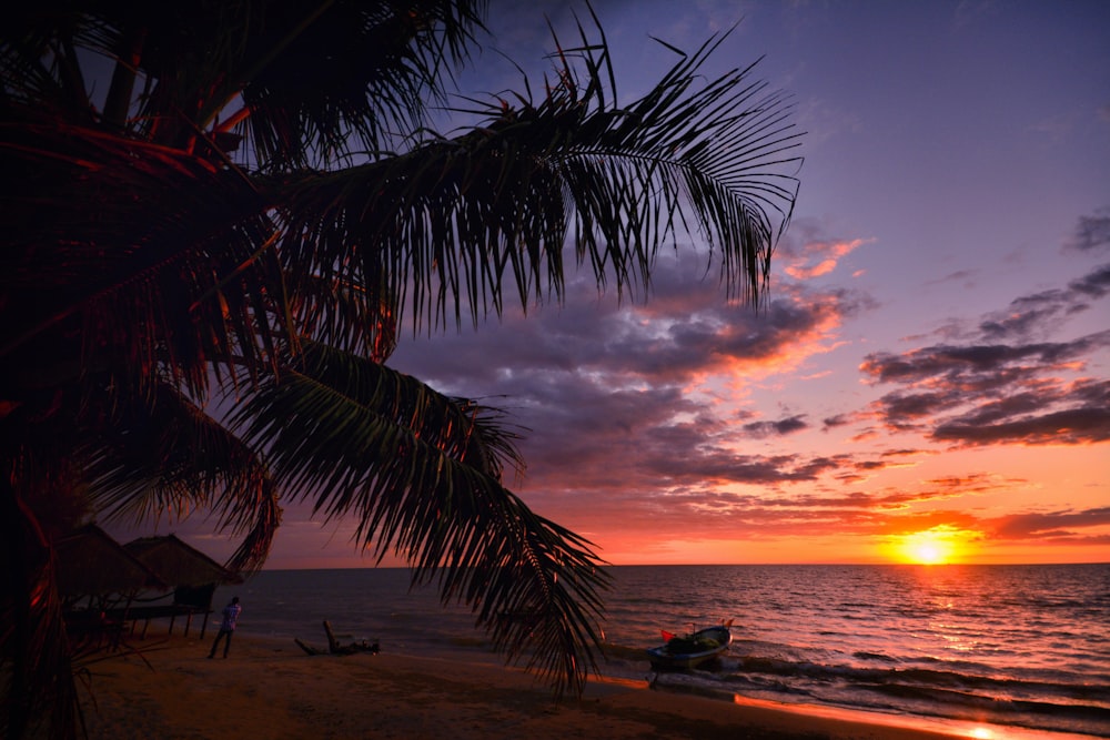 Una puesta de sol en una playa con un barco en el agua